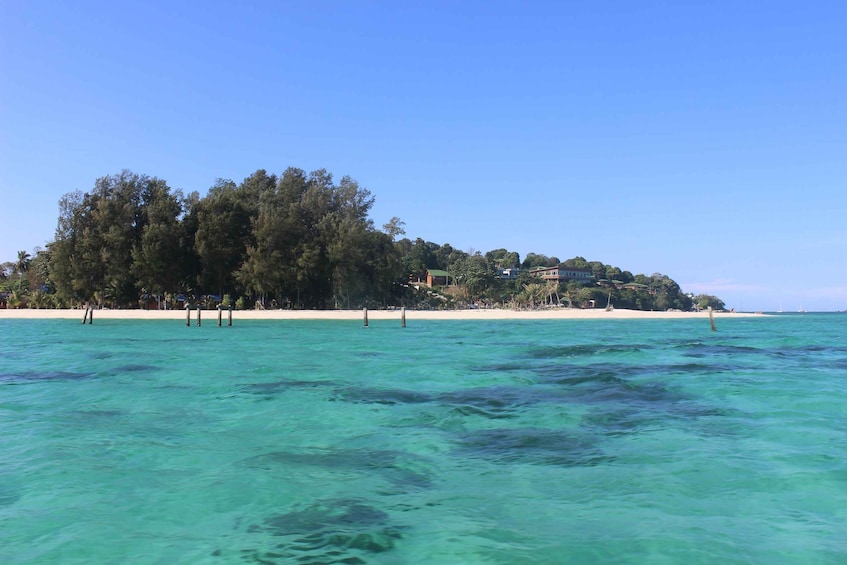 A beach with clear turquoise water, a small island with dense trees, and a building on the island. 3