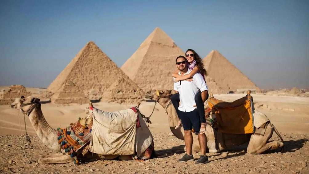 A person with a camel in a desert with pyramids in the background. 5