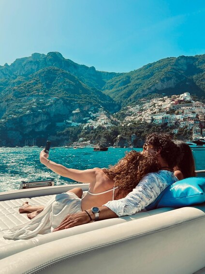 Two people on a boat taking a selfie with a coastal town and mountains in the background. 5