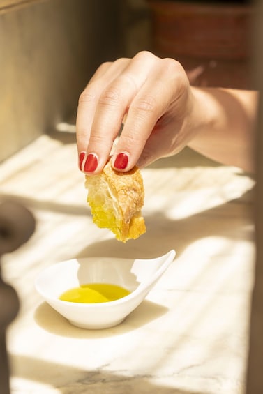 A hand dipping a piece of bread into a bowl of yellow liquid. 5