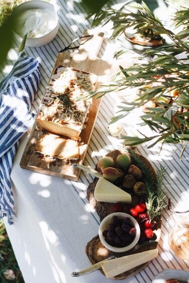 A picnic setup with a wooden board, cheese, olives, and a bowl of yogurt. 1