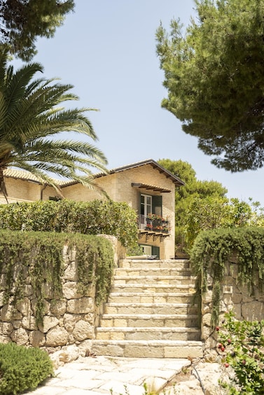 A stone staircase leading to a house with a balcony, surrounded by greenery and trees. 2