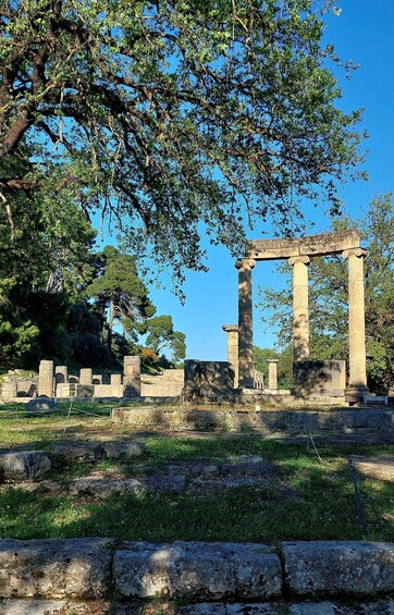 Ancient ruins with columns and stone structures, surrounded by trees and grass. 3
