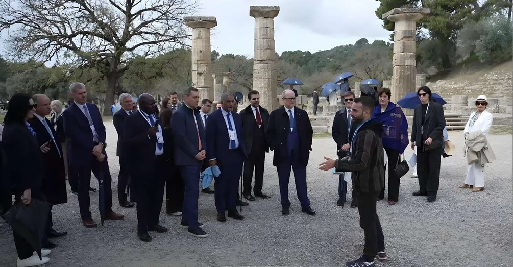 A group of formally dressed individuals standing outdoors near ancient stone columns. 5