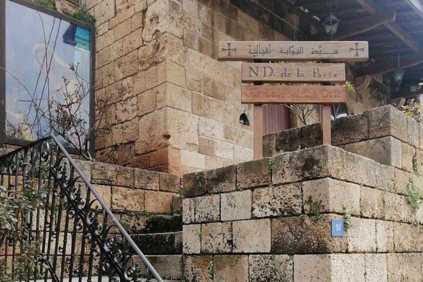 A stone wall with a sign reading 'N.D. de la Porte Our Lady of the Gate.' 2