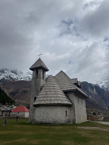 A stone church with a bell tower and a red-roofed building nearby. 5