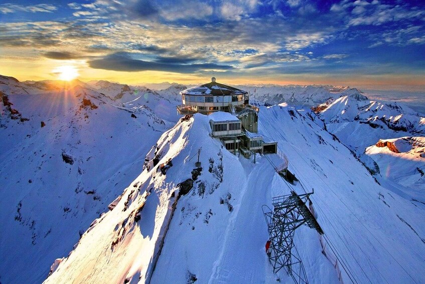 A snow-covered mountain peak with a circular observation tower and a power line structure. 3