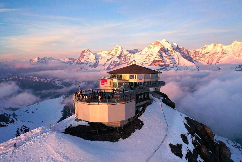 A snow-covered mountain peak with a viewing platform and a building with a red flag. 1