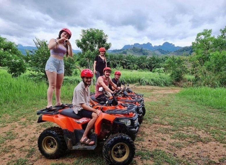 A group of people on an ATV in a grassy area with mountains in the background. 1
