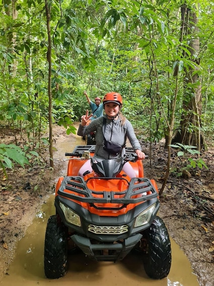 A person on an orange ATV in a forested area with muddy ground. 2