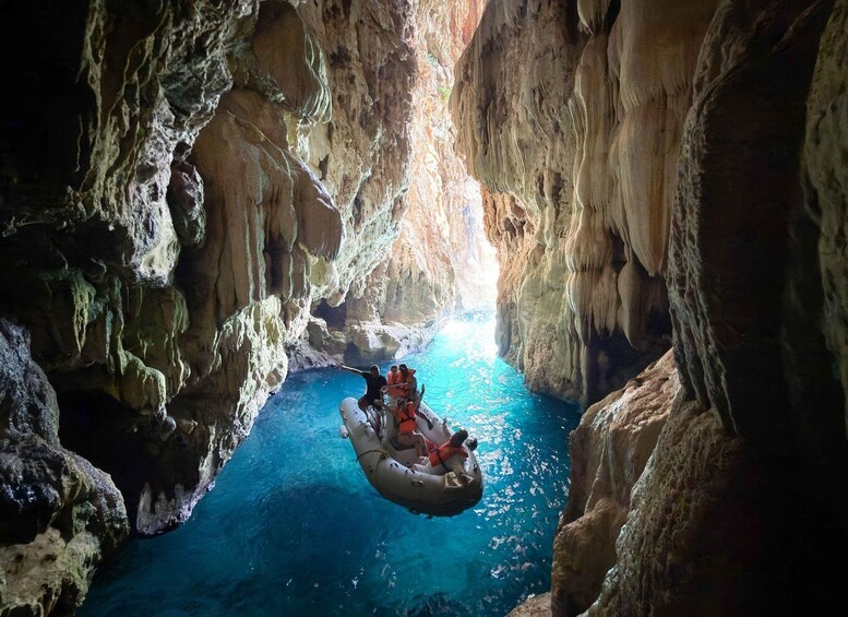 A raft navigating through a narrow, rocky cave with a clear blue water channel. 5