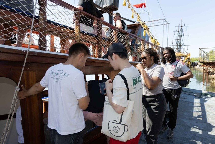 People on a wooden boat with a netted railing, docked near water. 2