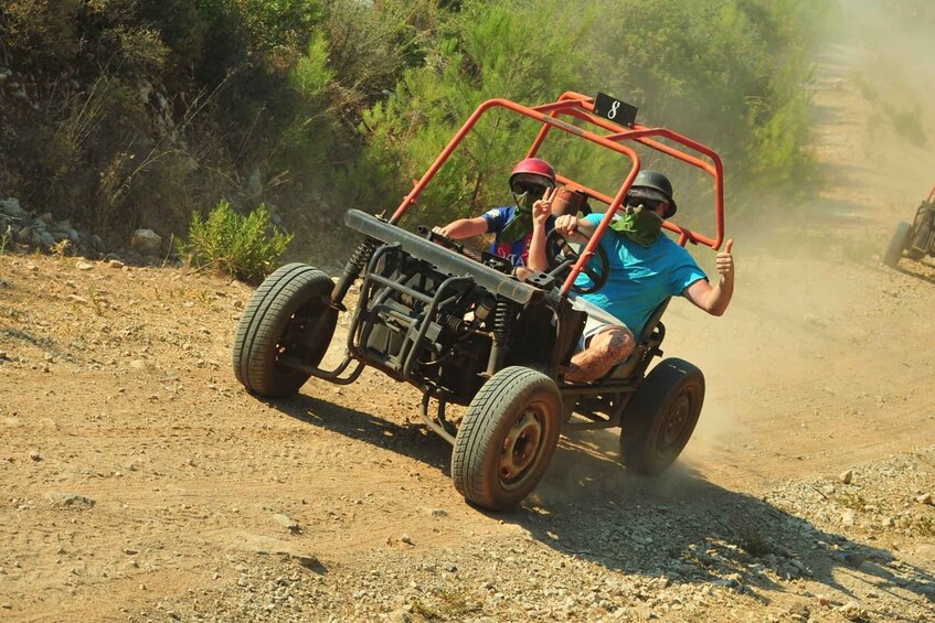 Two people in a dune buggy on a dirt path with sparse vegetation. 1