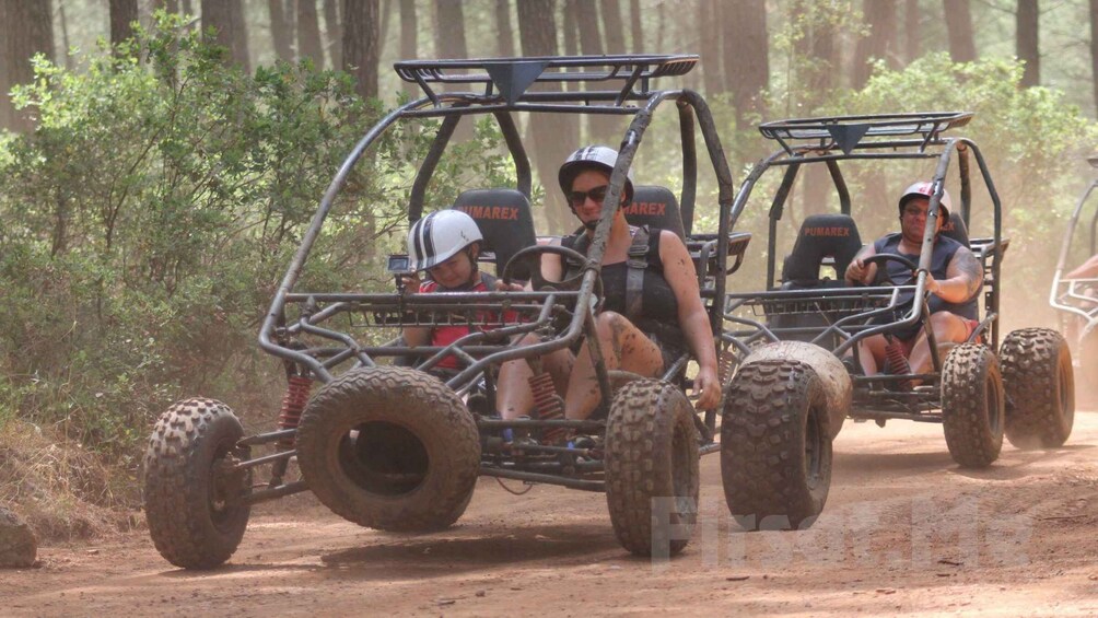 A four-wheeled off-road vehicle with passengers, traversing a dirt path in a forested area. 5