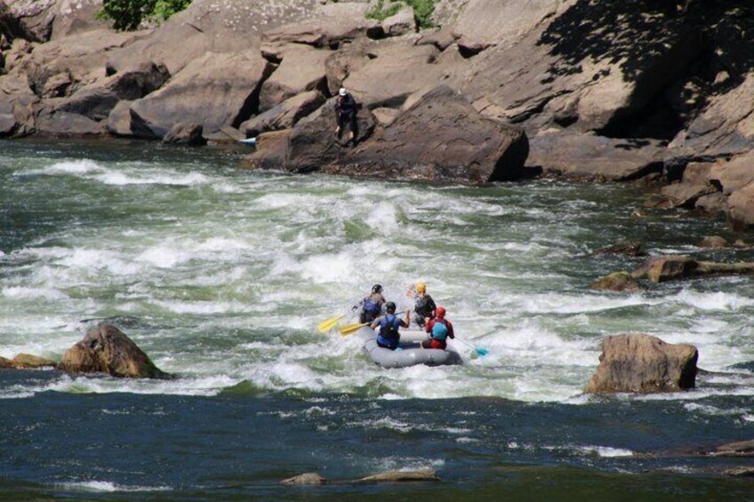 A group of people rafting on a river with rocky banks. 2