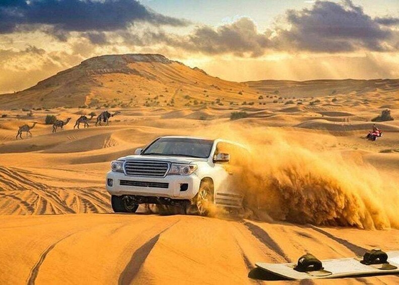 A white SUV driving through a desert with sand dunes and camels in the background. 1