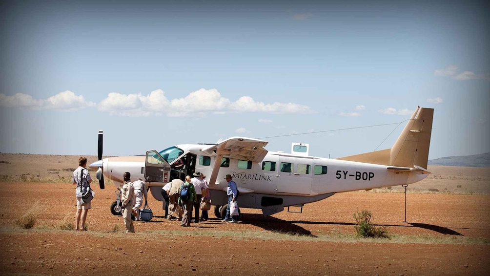 A small aircraft with passengers boarding, labeled 'SAFARILINK' and '5Y-BOP' on its side, in a desert setting. 1