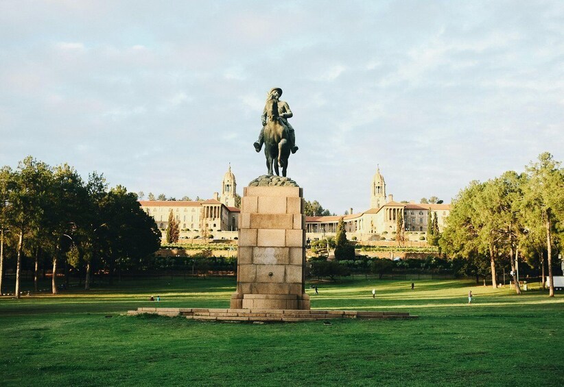 A statue of a man on horseback in a park with a large building in the background. 4