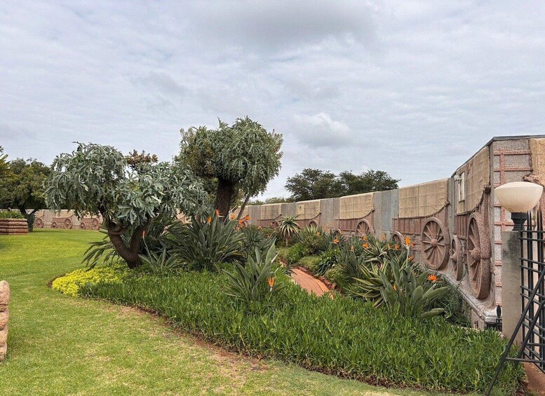 A garden with a large tree, a stone wall with decorative elements, and a street lamp. 3
