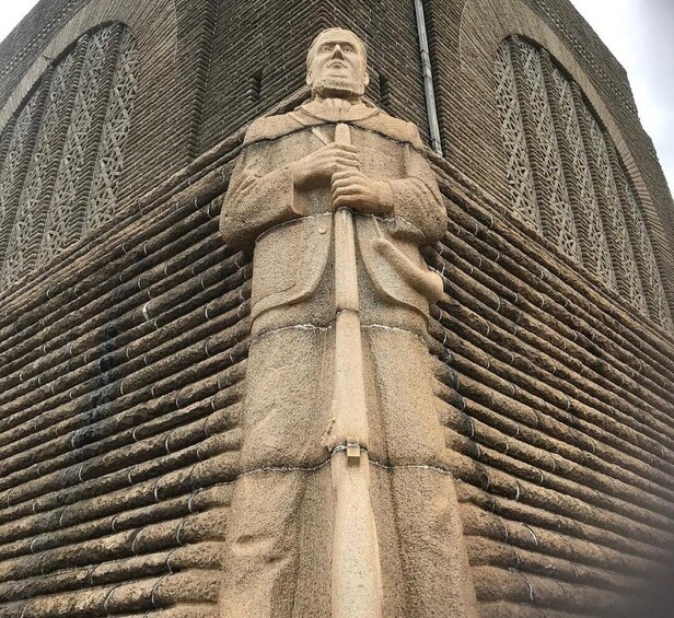 A large stone statue of a man holding a staff, set against a brick wall with intricate patterns. 2