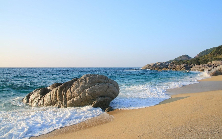A beach with a large rock formation in the water and a sandy shore. 1