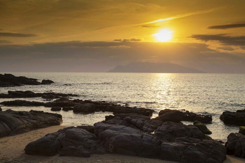 A sunset over a rocky coastline with calm waters reflecting the sun. 3