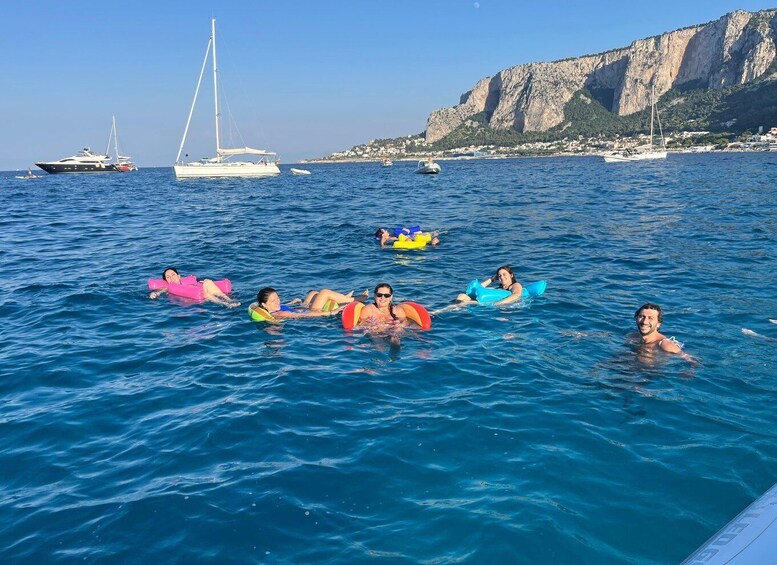 People floating on water with boats and a rocky cliff in the background. 4