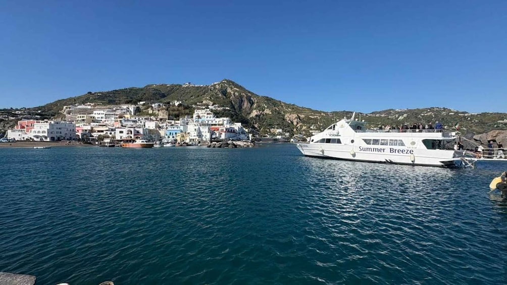 A white yacht named 'Summer Breeze' docked at a harbor with colorful buildings and a mountainous backdrop. 2