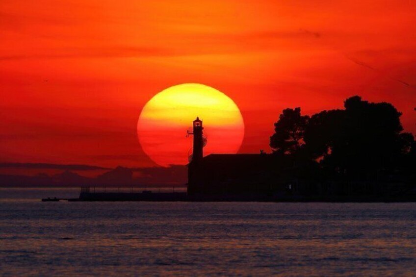 A sunset over a body of water with a lighthouse silhouette and trees. 2
