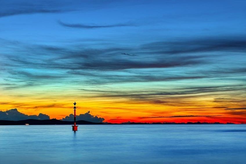 A sunset over a calm body of water with a buoy in the foreground and a silhouette of land in the distance. 4