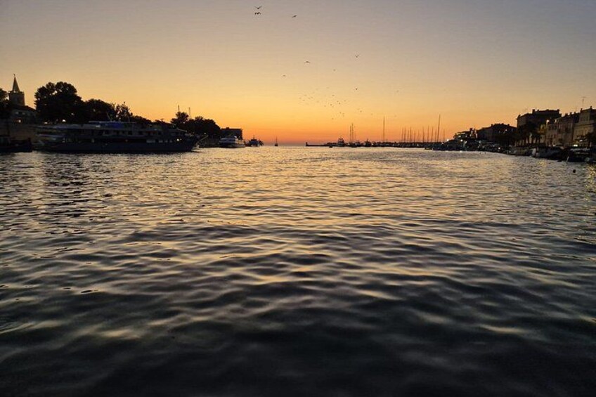 Un atardecer sobre un río tranquilo con barcos, edificios y un horizonte urbano distante. 3