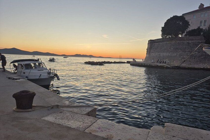 Un paisaje costero con barcos, un muro de piedra y una puesta de sol. 2