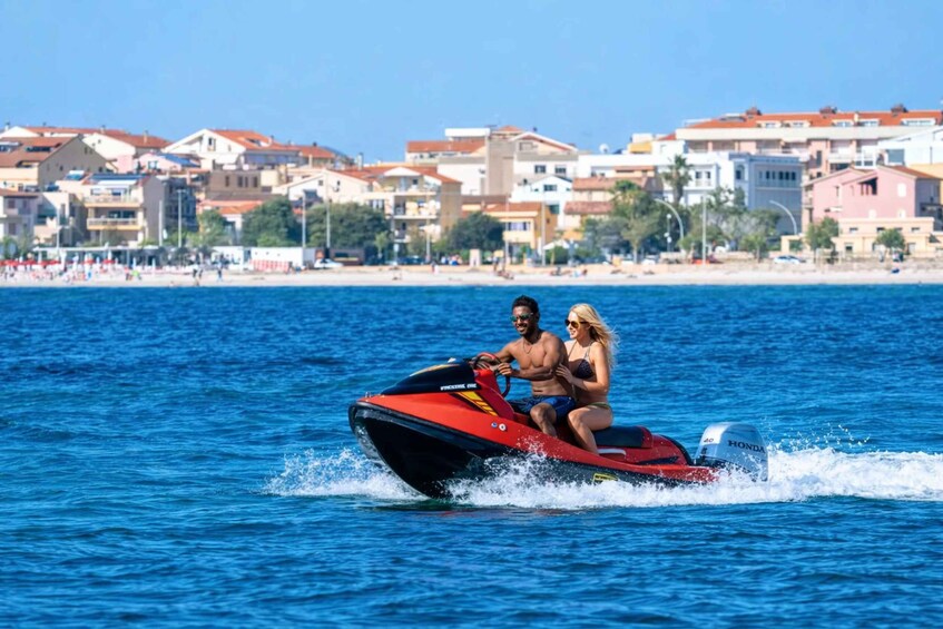A jet ski with two people on it, moving through the water with a coastal town in the background. 3