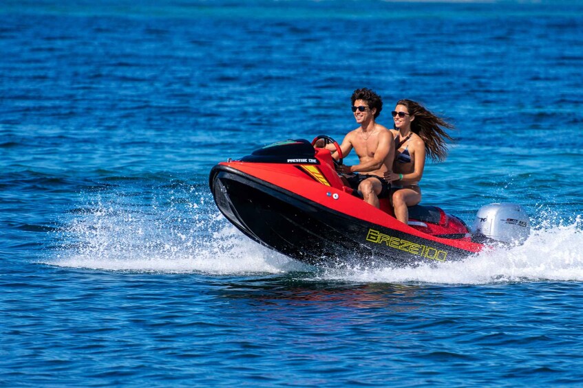 Two people on a red and black jet ski on a body of water. 2