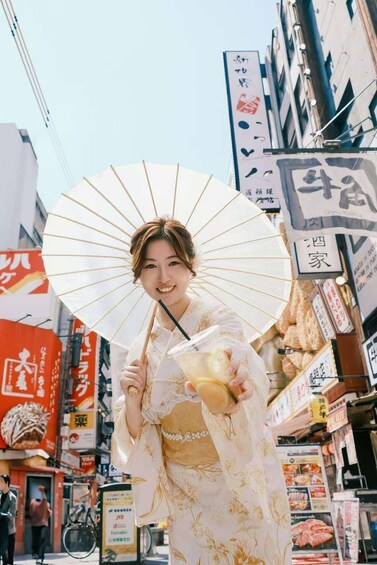 A person holding a fan and a drink in an urban setting with Japanese signage. 5