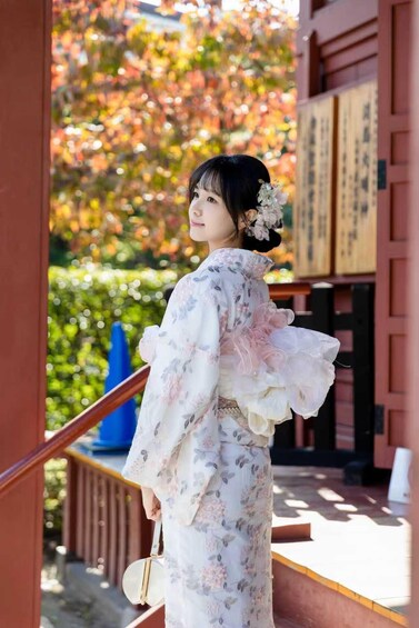 A person in a kimono with floral patterns, standing on a wooden staircase with a traditional building in the background. 3