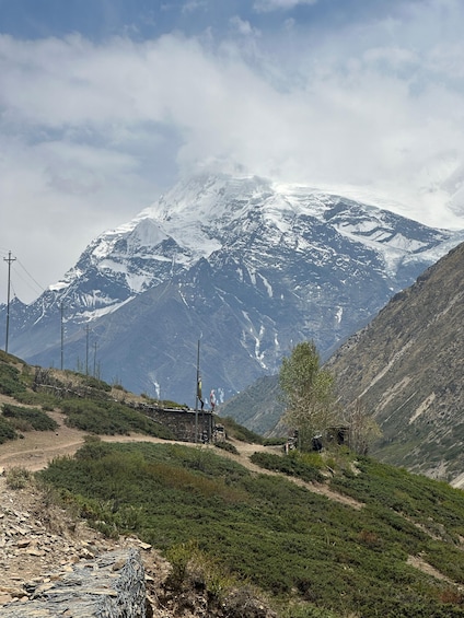 A mountainous landscape with a snow-capped peak, a dirt path, and a small structure. 3