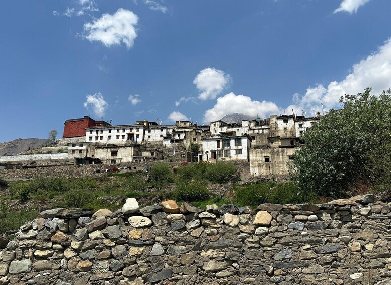 A mountainous village with traditional buildings, a prominent red structure, and a stone wall in the foreground. 4