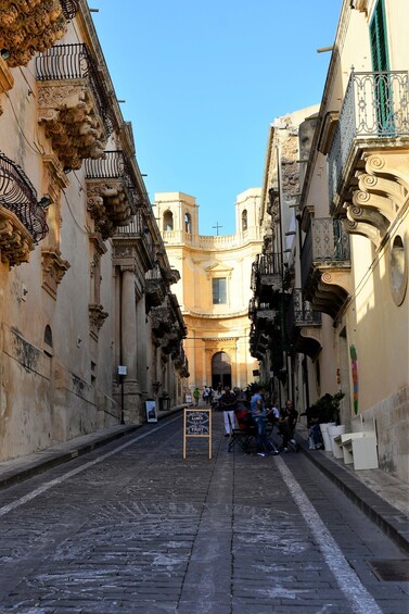 A cobblestone street lined with historic buildings, a signboard, and a group of people. 3