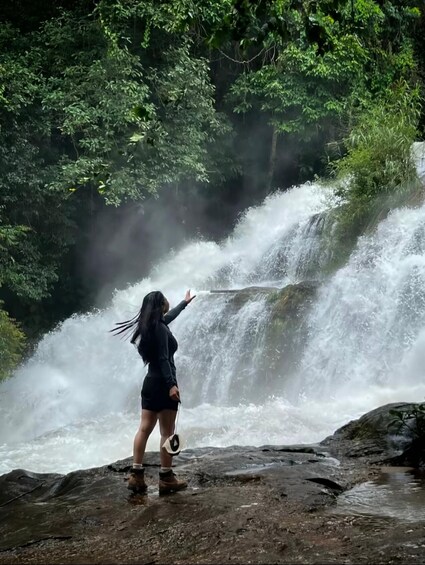 A person standing on rocks by a waterfall in a forest. 4