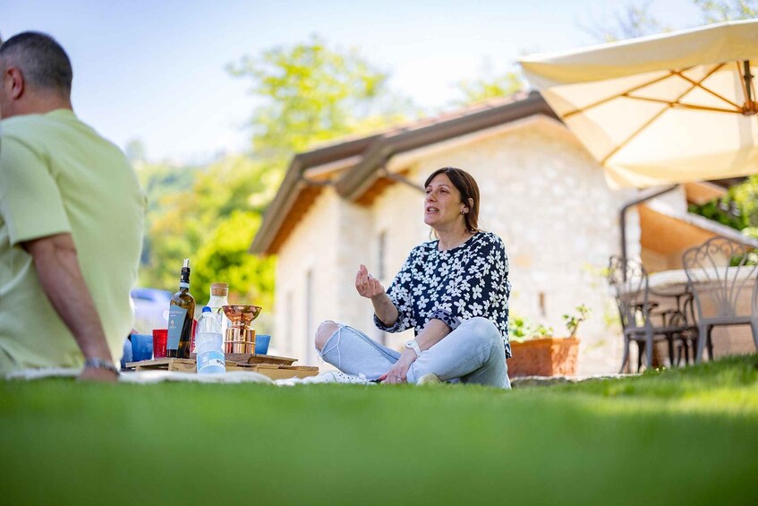 A person sitting on the grass with a bottle, a cup, and a plate, in a sunny outdoor setting. 5