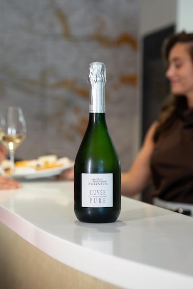 A bottle of Cuvée Pure wine on a table with a blurred background of a person. 2