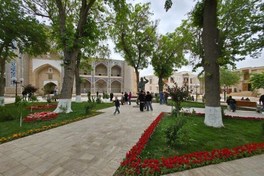 A courtyard with trees, red flowers, and people walking. 1