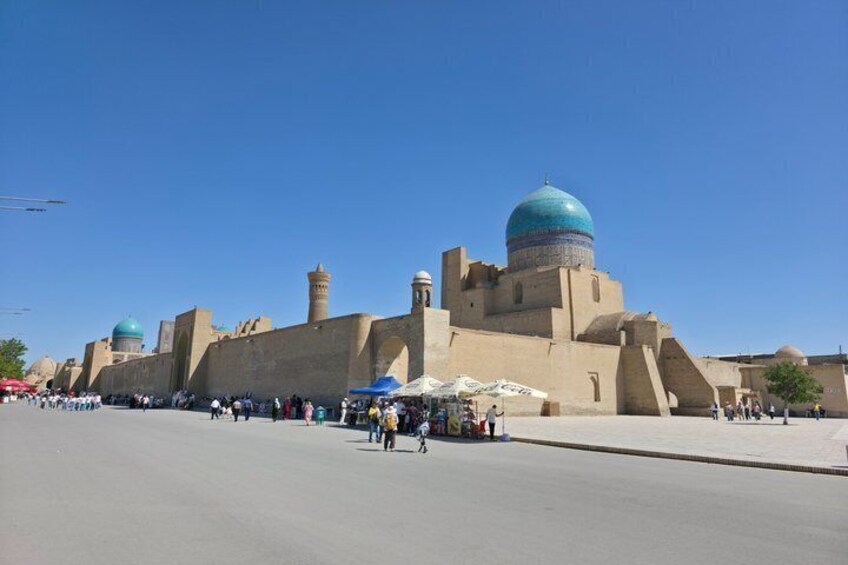A large mosque with a prominent blue dome and minarets, surrounded by a paved area with people and tents. 2
