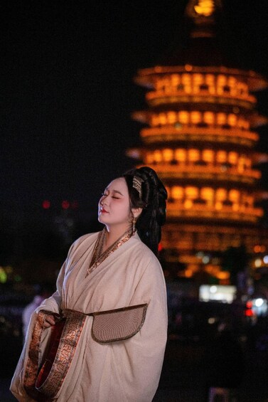 A person in traditional attire standing with a guitar, a pagoda-style building in the background. 2