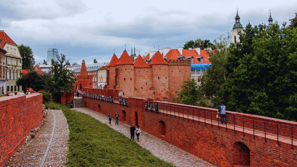A historic brick wall with a bridge, red-roofed buildings, and a tower in the background. 5