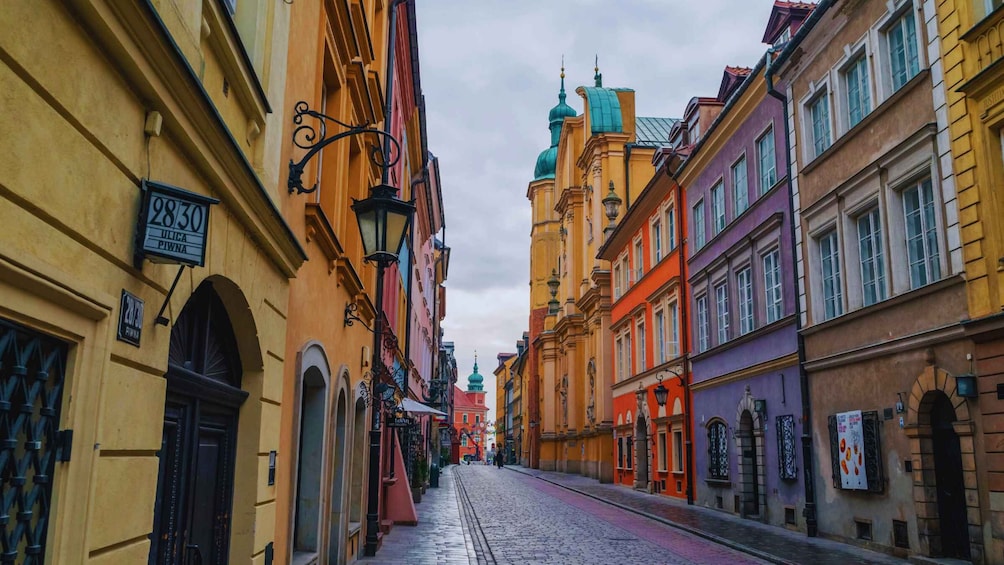 A cobblestone street lined with colorful buildings, a church with a green dome, and street lamps. 4