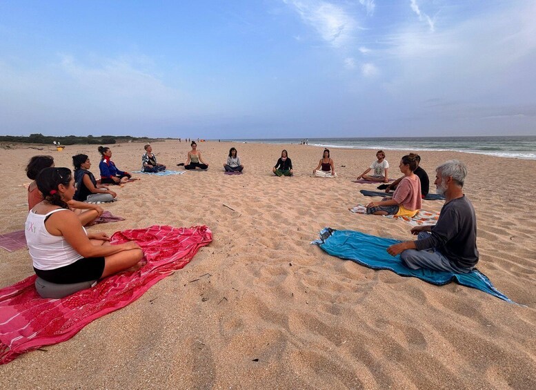 A group of people sitting in a circle on a beach, engaged in a meditation or yoga session. 4