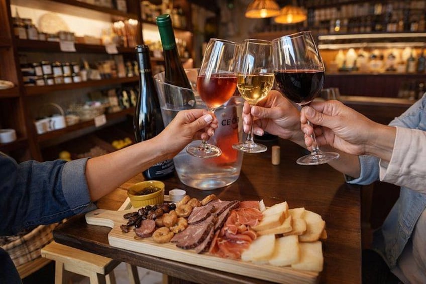 A person toasting with wine glasses, a bottle of wine, and a charcuterie board with meats and cheeses. 4