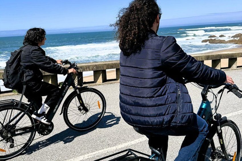 Two people riding bicycles on a coastal road with the ocean in the background. 1